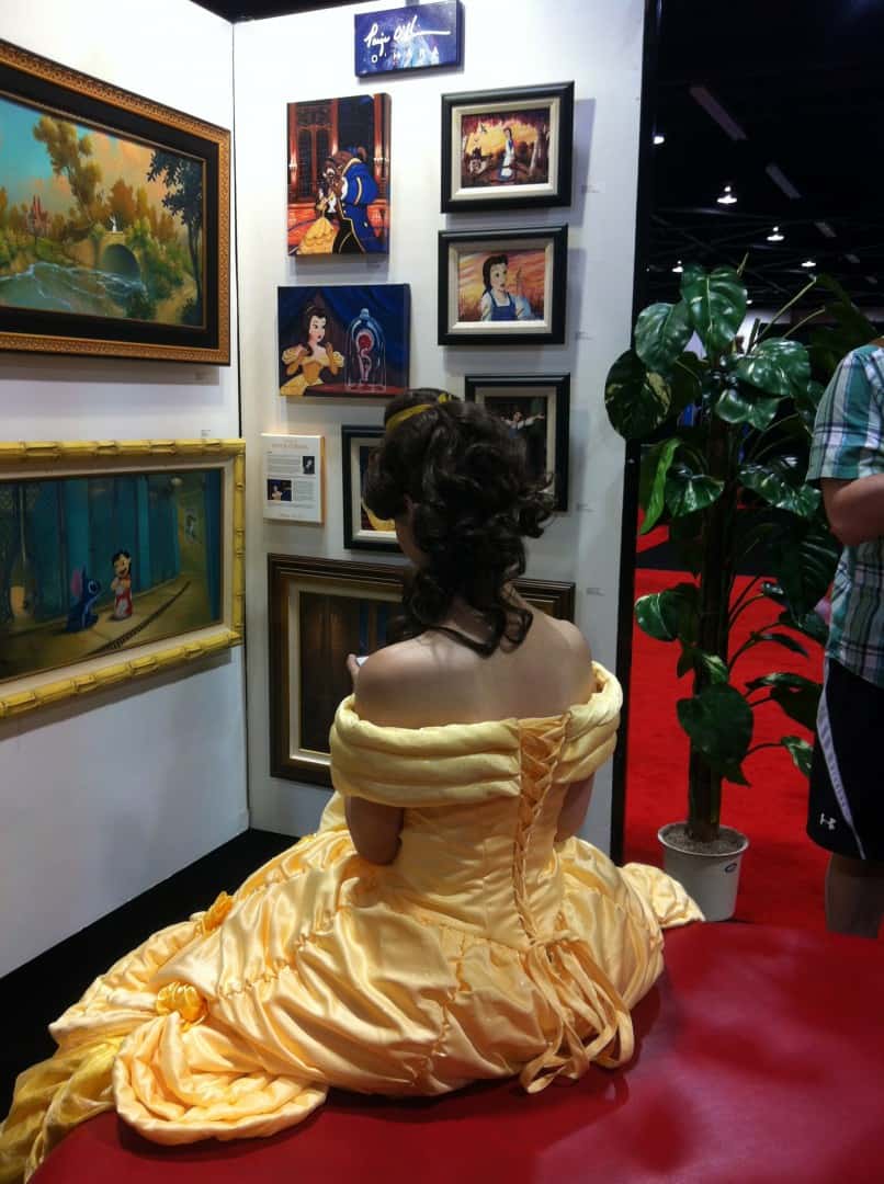 Belle texting in front of the 'Beauty and the Beast' art display.